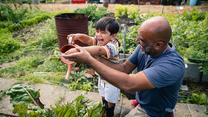 Hombre ayudando a un niño sonriente a regar plantas en un jardín