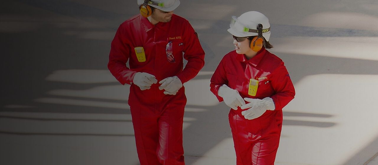 Trabajador y trabajadora con overoles rojos, cascos blancos y protección auditiva caminando