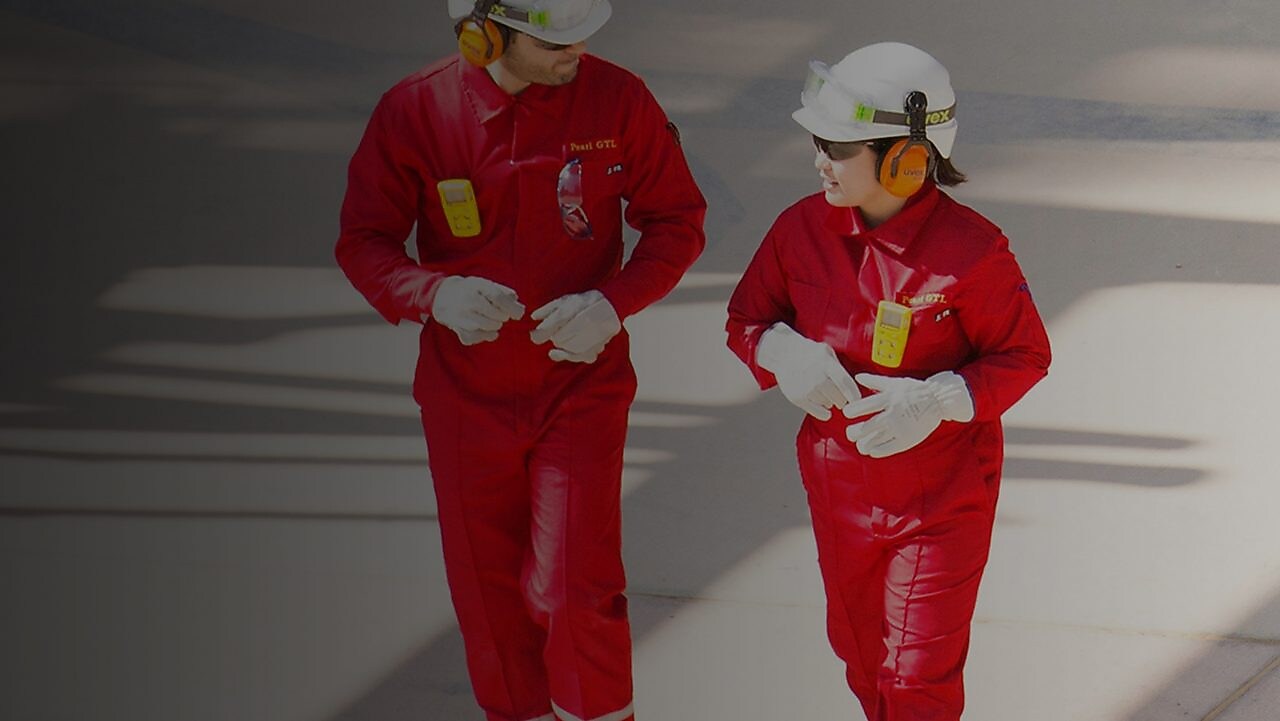 Trabajador y trabajadora con overoles rojos, cascos blancos y protección auditiva caminando