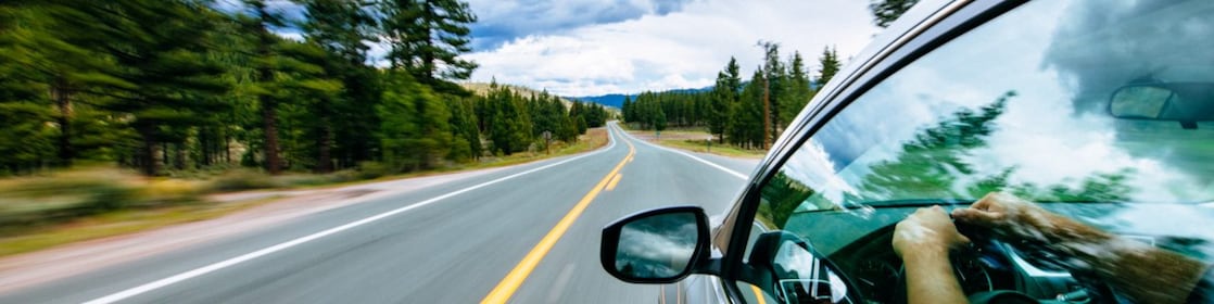 Hombre manejando un vehículo por una carretera larga rodeada de árboles.
